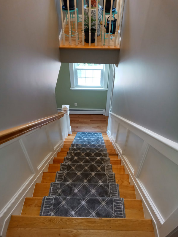 Pine wood flooring installation on stairs and balcony in stairwell with white and green walls. Stairs have a gray runner along wood floors.